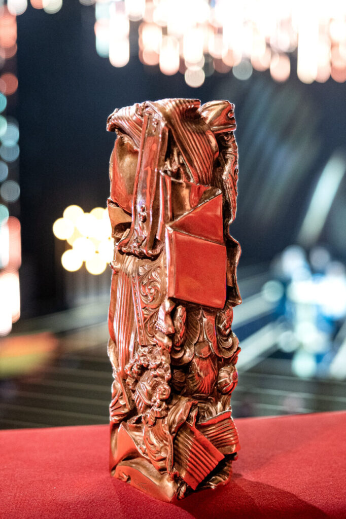 Estatuilla de Premios César encima de un fieltro rojo y fondo oscuro.